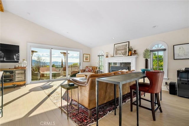 living room featuring plenty of natural light, light wood-style floors, a high end fireplace, and vaulted ceiling