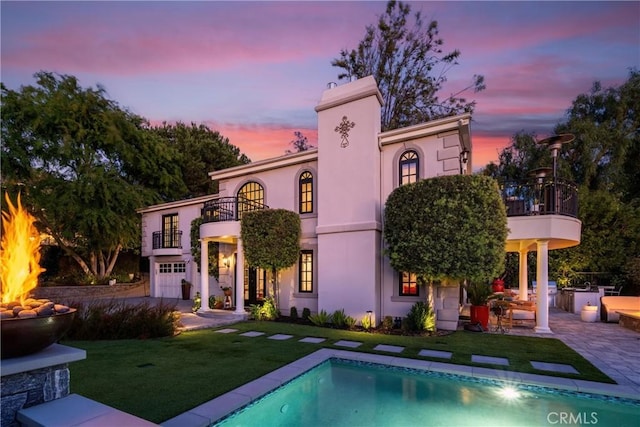 back of property at dusk with a patio area, a yard, a balcony, and stucco siding