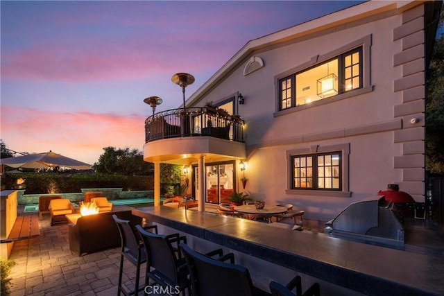 view of patio / terrace with outdoor wet bar, a fire pit, an outdoor pool, a balcony, and an outdoor kitchen