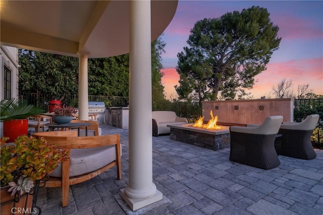 patio terrace at dusk with grilling area, a fire pit, an outdoor kitchen, and fence