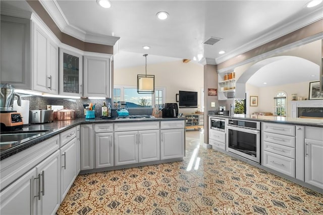 kitchen featuring dark countertops, open floor plan, ornamental molding, appliances with stainless steel finishes, and a peninsula