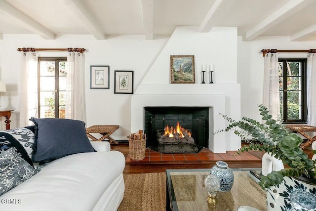 living area featuring beamed ceiling, a large fireplace, and wood finished floors