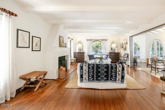 living room with beamed ceiling, a large fireplace, and wood finished floors