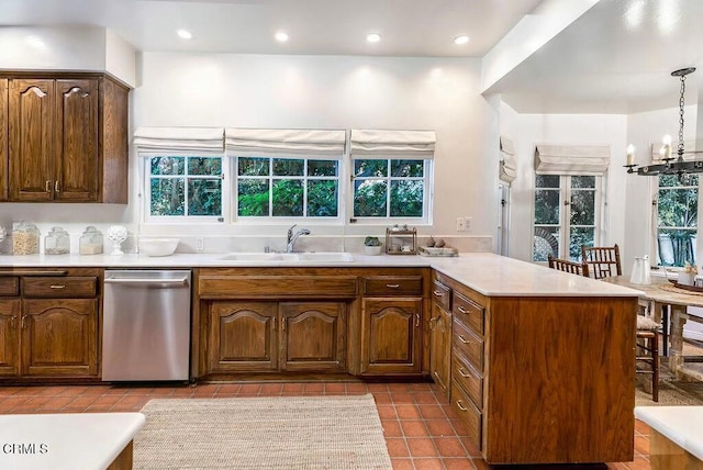 kitchen featuring pendant lighting, light countertops, a peninsula, stainless steel dishwasher, and a sink