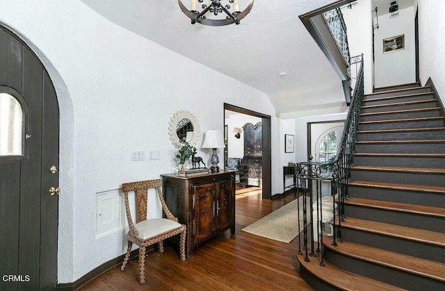 entrance foyer with arched walkways, stairway, lofted ceiling, and wood finished floors