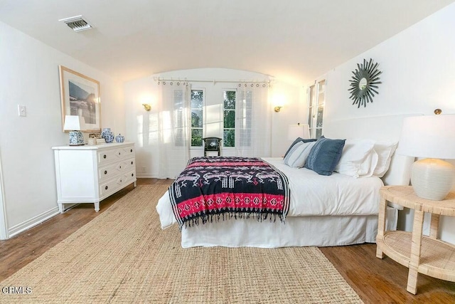 bedroom featuring lofted ceiling, wood finished floors, visible vents, and baseboards