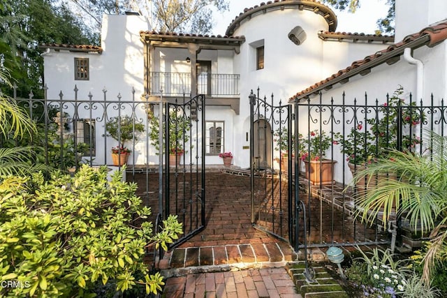 exterior space featuring fence, a tile roof, stucco siding, a balcony, and a gate