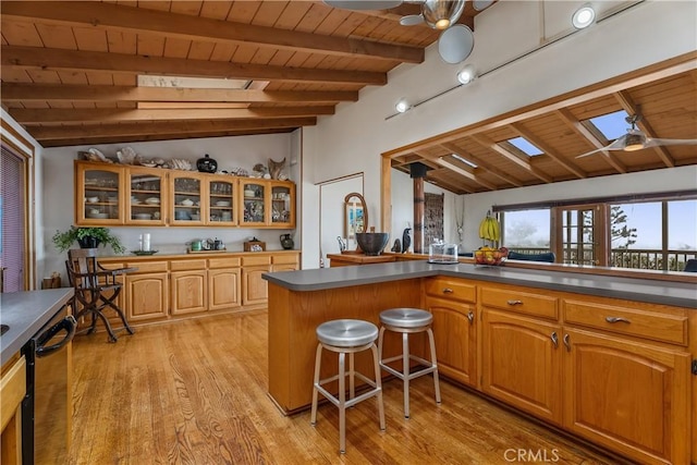 kitchen featuring dark countertops, glass insert cabinets, dishwasher, vaulted ceiling with skylight, and a ceiling fan