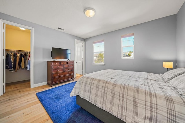 bedroom featuring wood finished floors, visible vents, baseboards, a spacious closet, and a closet