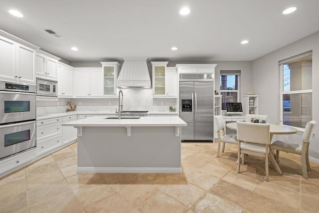 kitchen with a sink, light countertops, custom range hood, white cabinets, and built in appliances