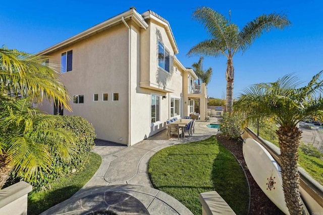 rear view of house featuring stucco siding, a patio, a balcony, and a fenced in pool