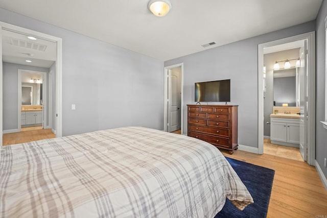 bedroom with visible vents, connected bathroom, baseboards, and light wood-style floors