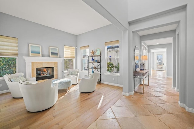 living room with a wealth of natural light, baseboards, light wood-style floors, and a tile fireplace