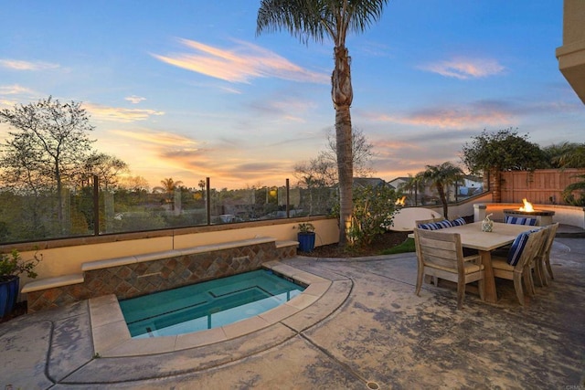 pool at dusk featuring outdoor dining space, an in ground hot tub, a patio, and fence