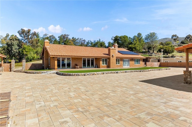 rear view of property featuring fence, solar panels, stucco siding, a chimney, and a tile roof