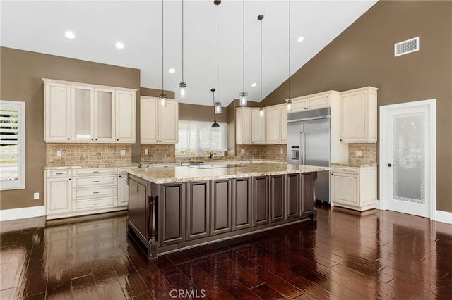 kitchen with visible vents, light stone counters, a spacious island, built in fridge, and dark wood-style flooring