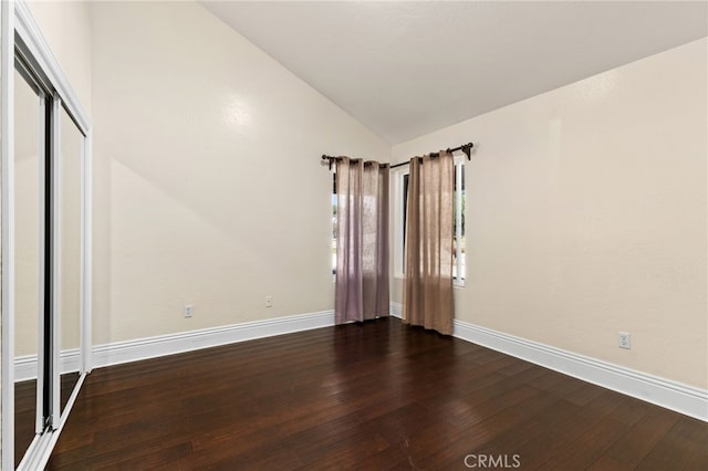 spare room with baseboards, lofted ceiling, and dark wood finished floors