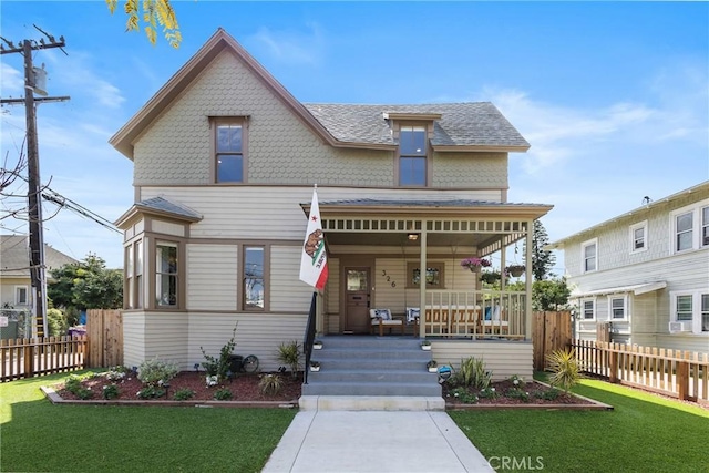 victorian-style house featuring a front lawn, fence, covered porch, and a shingled roof