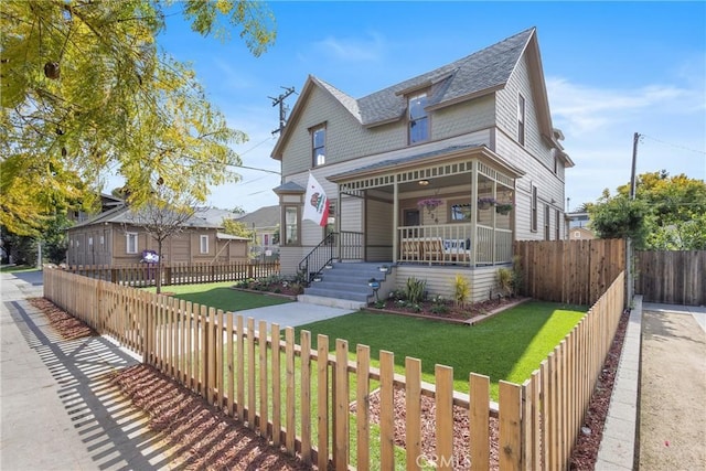 victorian home featuring a front yard, covered porch, a fenced front yard, and roof with shingles