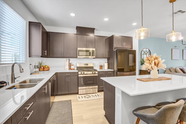 kitchen featuring a breakfast bar area, a sink, dark brown cabinetry, light countertops, and appliances with stainless steel finishes