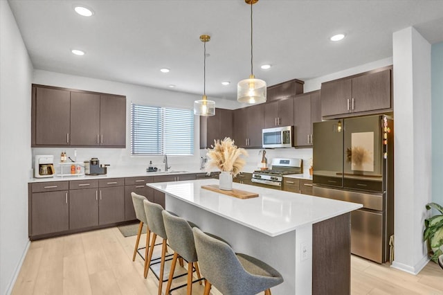 kitchen with light wood finished floors, dark brown cabinets, light countertops, appliances with stainless steel finishes, and a sink