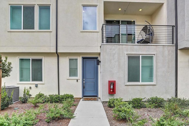 entrance to property featuring a balcony, stucco siding, and central AC