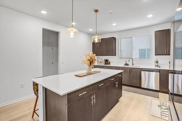 kitchen with a sink, stainless steel dishwasher, light countertops, and light wood finished floors