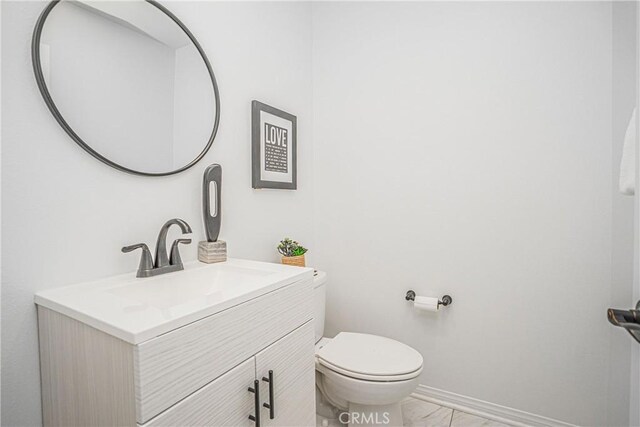 bathroom with vanity, toilet, baseboards, and marble finish floor