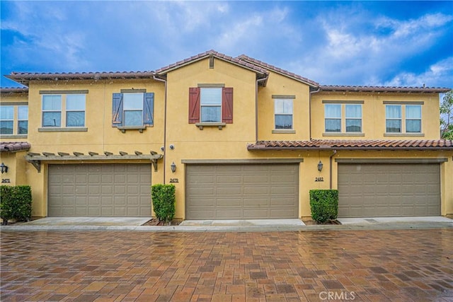 townhome / multi-family property with stucco siding, driveway, an attached garage, and a tile roof