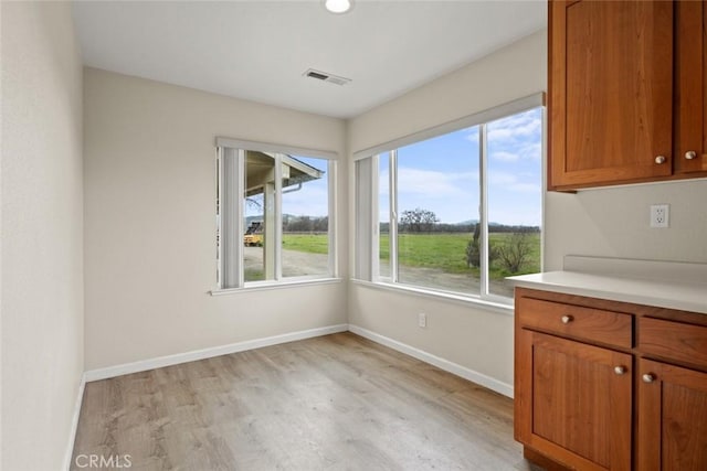 unfurnished dining area featuring light wood-type flooring, visible vents, and baseboards