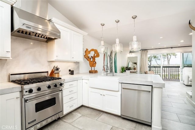 kitchen featuring appliances with stainless steel finishes, light countertops, wall chimney exhaust hood, and a peninsula