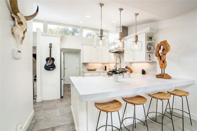 kitchen with white cabinetry, a peninsula, wall chimney exhaust hood, and a kitchen bar