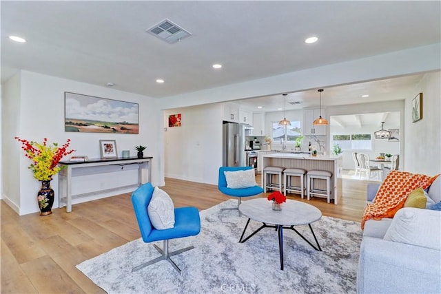 living room with recessed lighting, visible vents, light wood-style flooring, and baseboards