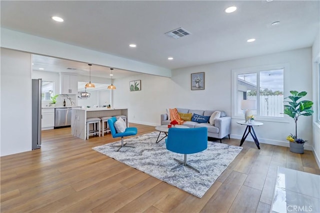 living room with recessed lighting, light wood-type flooring, baseboards, and visible vents