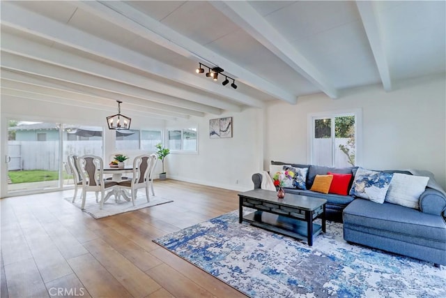 living room featuring an inviting chandelier, beamed ceiling, wood finished floors, and baseboards