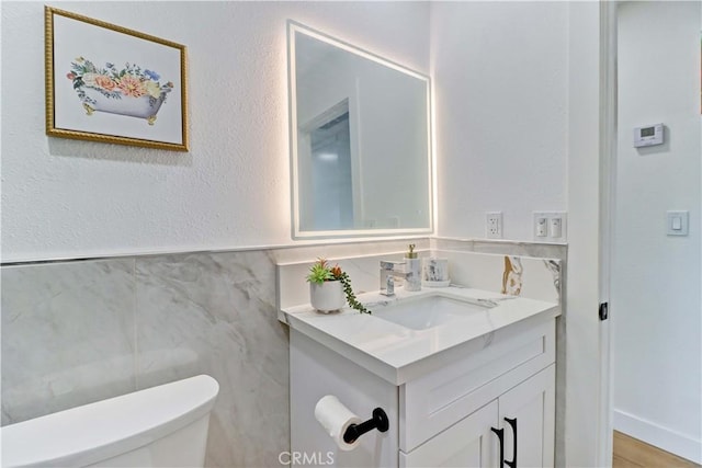 half bathroom featuring vanity, toilet, and a textured wall