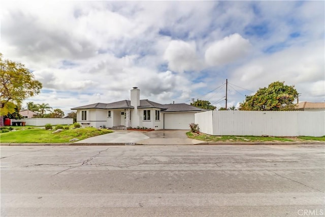 view of front facade featuring a chimney, concrete driveway, a garage, and fence