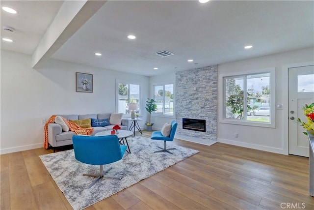 living area featuring visible vents, baseboards, a stone fireplace, recessed lighting, and wood finished floors