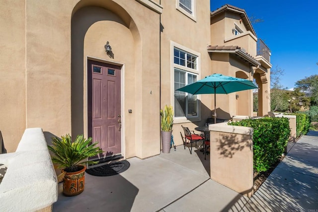 entrance to property with stucco siding, a tiled roof, and a patio