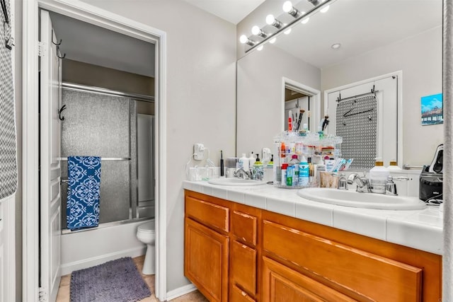 full bathroom featuring double vanity, bath / shower combo with glass door, toilet, and a sink