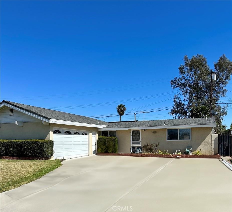 single story home with stucco siding, an attached garage, driveway, and fence