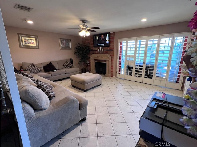 living room with light tile patterned floors, visible vents, a large fireplace, and a ceiling fan