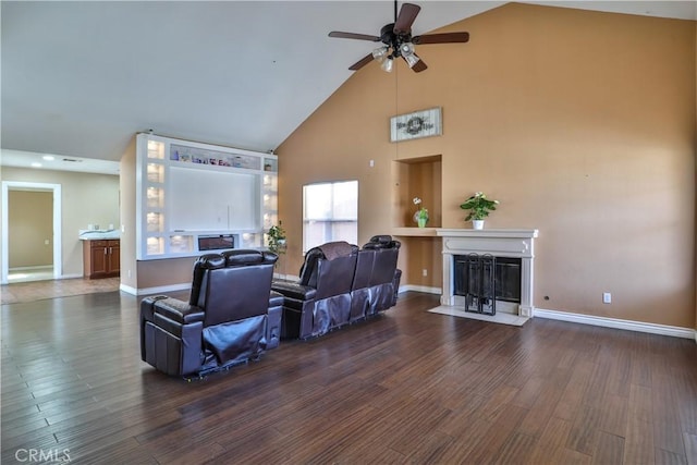 living area featuring a fireplace with flush hearth, high vaulted ceiling, wood finished floors, baseboards, and ceiling fan