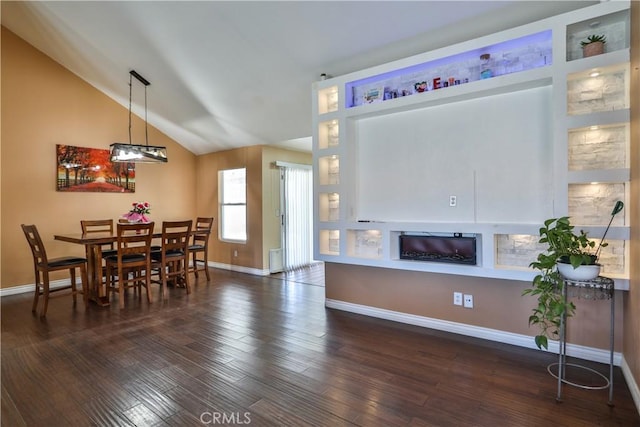 dining area with baseboards, lofted ceiling, dark wood-type flooring, and a glass covered fireplace