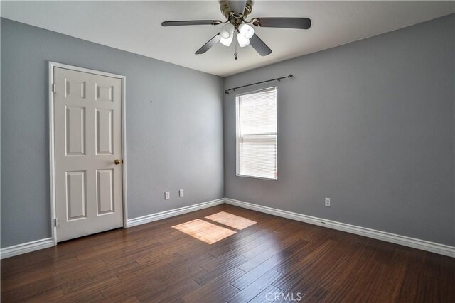 empty room with baseboards, a ceiling fan, and dark wood-style flooring