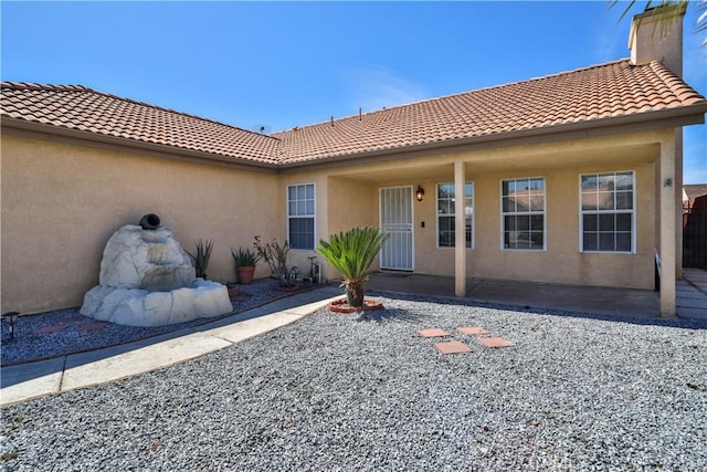 exterior space featuring stucco siding, a tiled roof, and a chimney