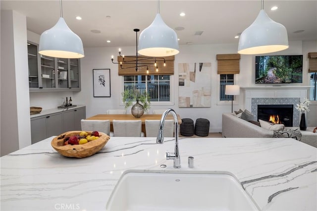 kitchen featuring gray cabinets, a sink, recessed lighting, glass insert cabinets, and light stone countertops