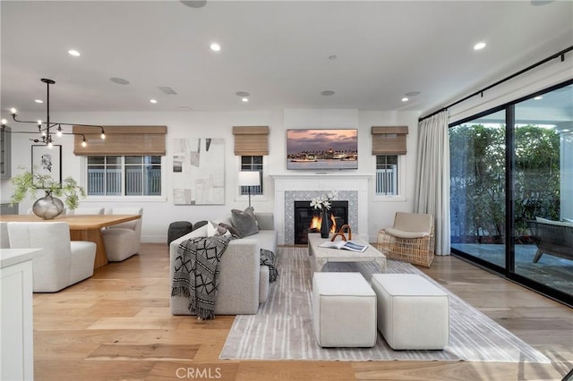 living room with a notable chandelier, recessed lighting, light wood-type flooring, and a premium fireplace