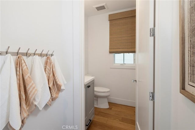 bathroom with vanity, wood finished floors, visible vents, baseboards, and toilet