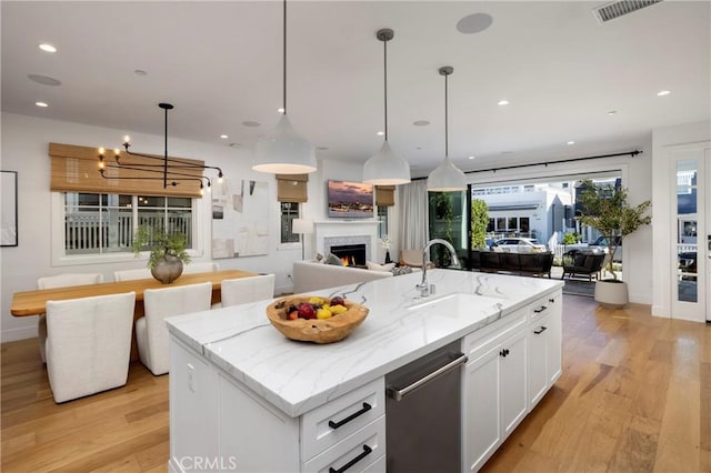 kitchen with open floor plan, light wood-style flooring, a warm lit fireplace, white cabinetry, and a sink